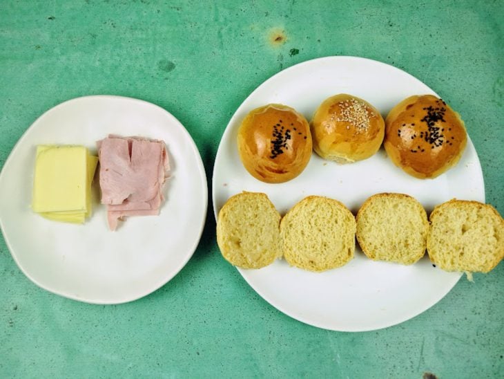 Pratos com presunto, queijo e pães fatiados ao meio.