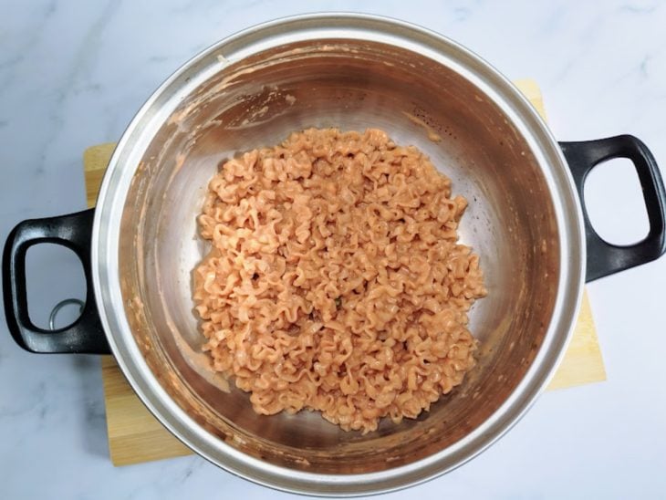Uma panela com miojo, tempero e requeijão.
