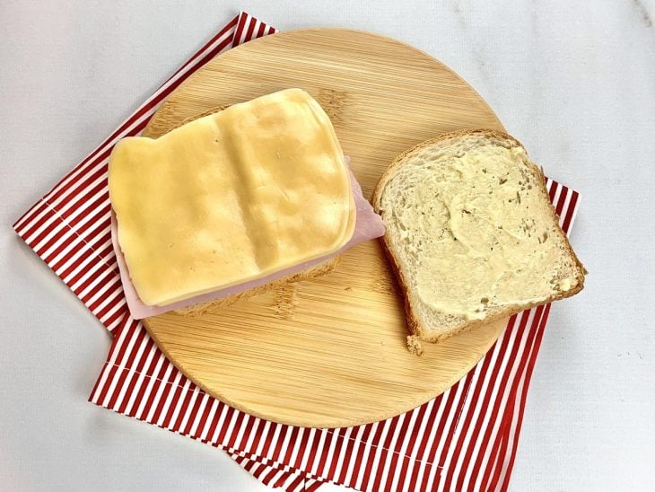 Uma fatia de pão com manteiga e outra fatia com presunto e queijo.