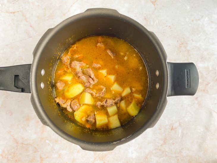 Batatas sendo adicionadas na panela de pressão, com a moela e os temperos.