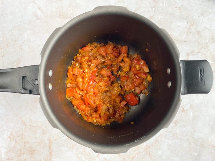 Cebola, alho, tomates e temperos em uma panela de pressão.
