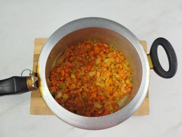 Uma panela de pressão com azeite, cebola, alho, salsão, cenoura e colorau.