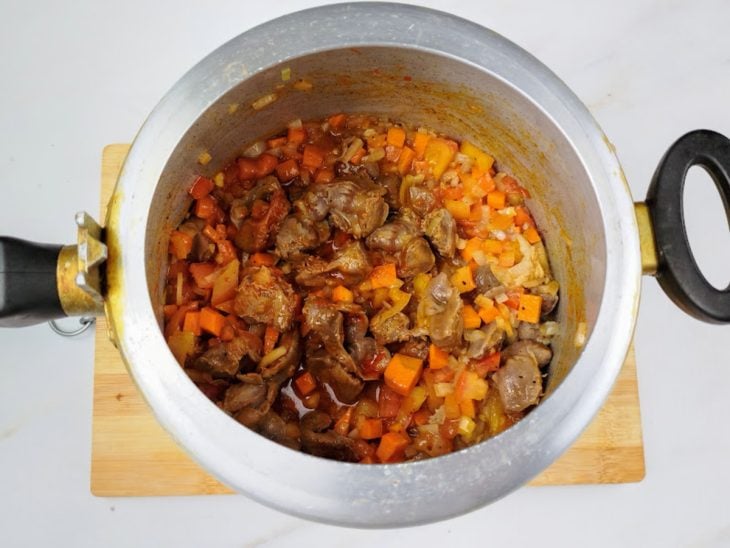 Uma panela com azeite, moela, cebola, alho, cenoura, tomates, cominho, páprica, mostarda em pó e louro.