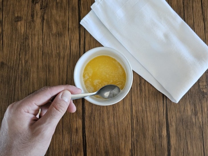 Manteiga derretida dentro do potinho com uma colher retirando as partes brancas.