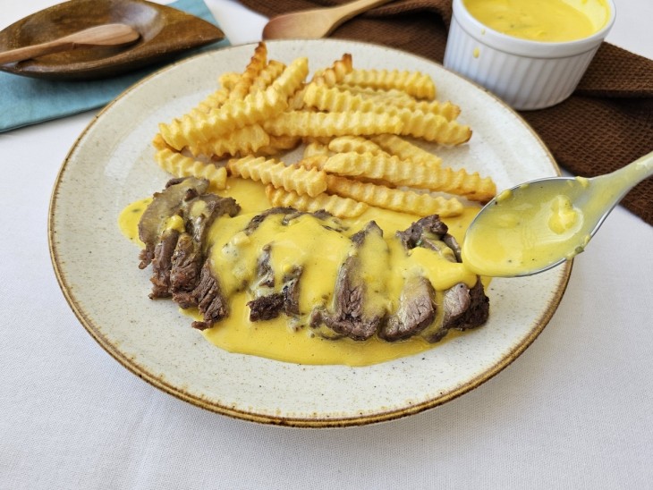 Molho béarnaise colocado por cima da carne e batata frita ao lado.