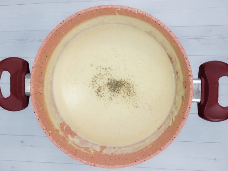 Uma panela com molho branco para lasanha e pimenta-do-reino.