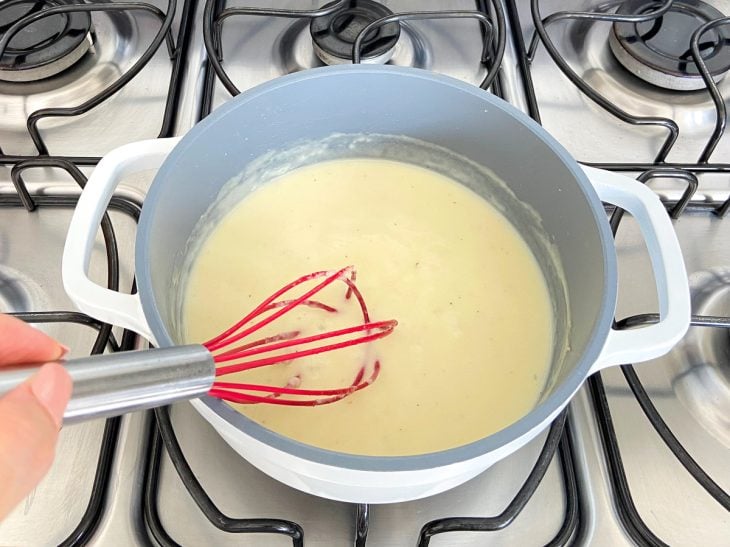 Uma panela contendo creme branco cozinhando e sendo temperado.