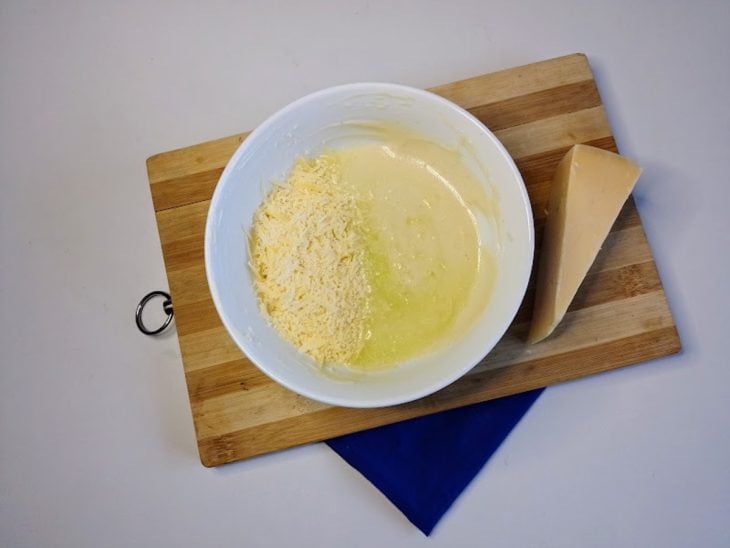 Um recipiente com queijo ralado, suco de limão, iogurte grego, mostarda e azeite.