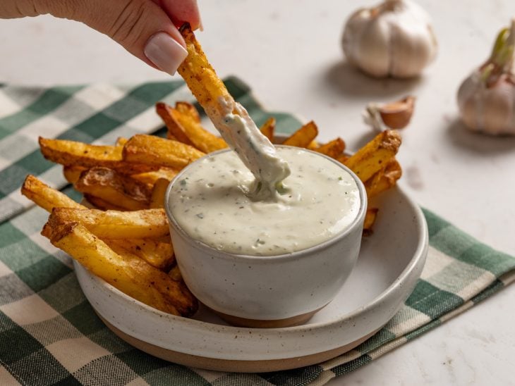 Molho de alho pronto para consumo ao lado de uma porção de batatas-fritas.
