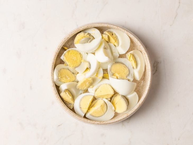 Ovos cozidos cortados ao meio, creme de leite, sal, dentes de alho amassado, azeite e cheiro-verde em um prato.