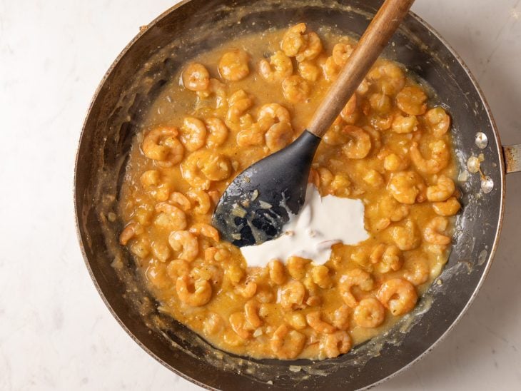 Uma frigideira com cebola, alho, manteiga, farinha, caldo de legumes, azeite de dendê e leite de coco.