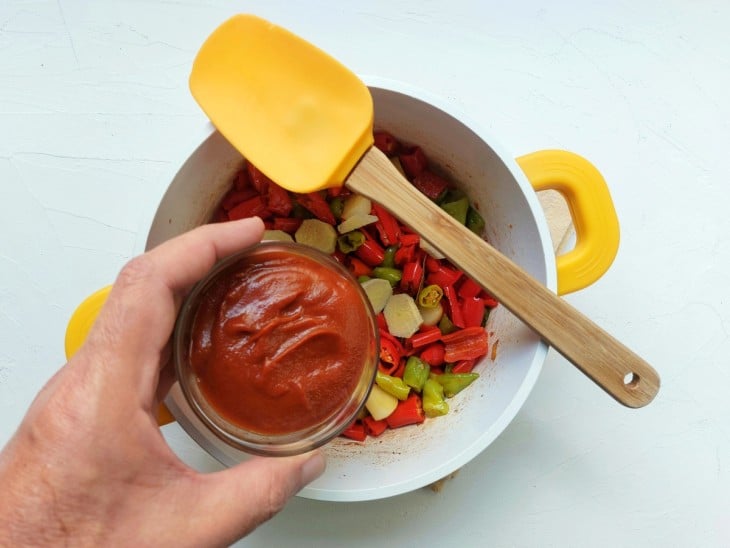 Uma panela com refogado de piemntas com molho de tomate.