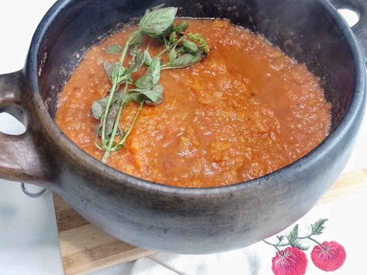 Uma panela contendo molho de tomate e folhas de manjericão.