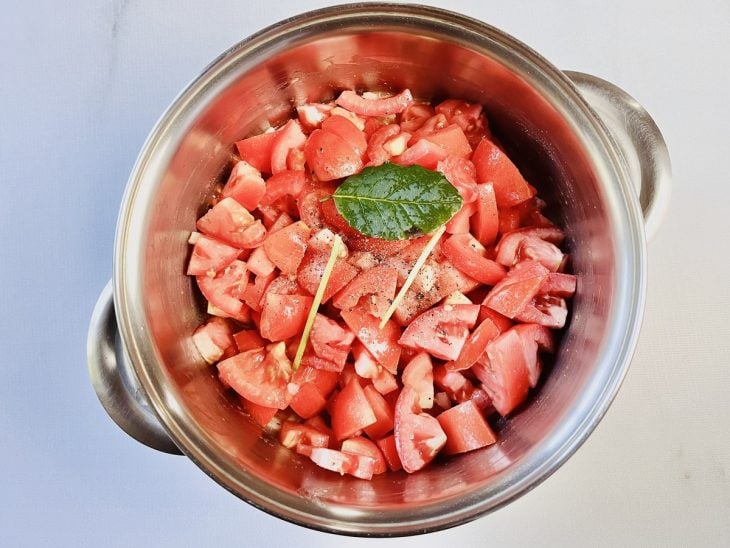 Tomates em cubos, folha de manjericão, sal e pimenta-do-reino adicionados na panela com alho e cebola refogados.