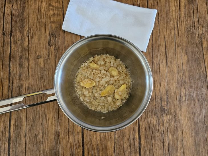 Uma panela refogando cebola e gengibre.