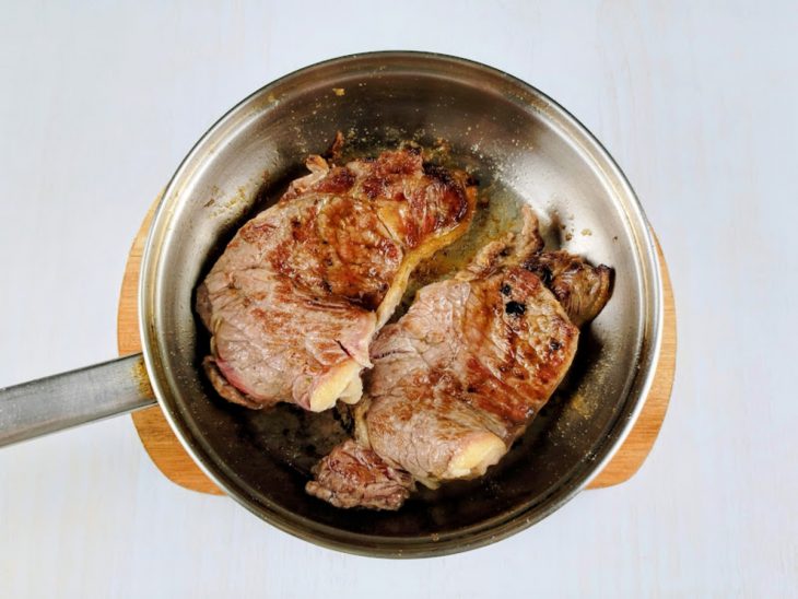 Carne temperada grelhada numa frigideira com azeite.