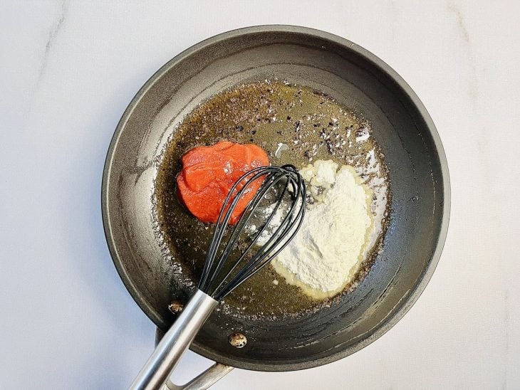 Extrato de tomate e farinha adicionados na frigideira com manteiga derretida.