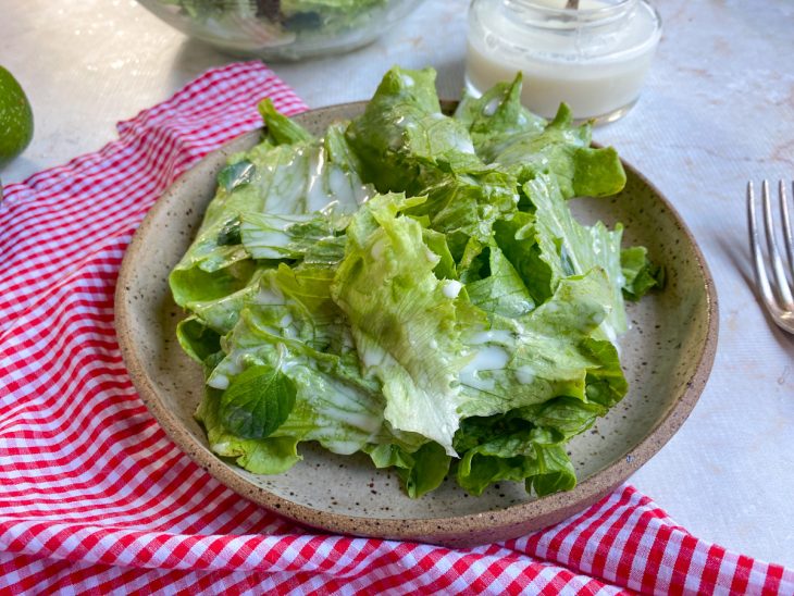 Molho para salada com iogurte natural e mel despejado sobre as folhas verdes.