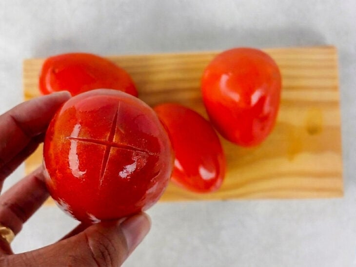 Tomates recebendo cortes em formato de cruz na parte inferior.