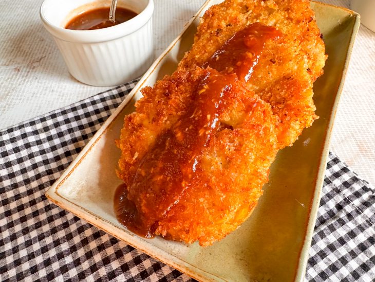 Molho sendo servido sobre uma porção de lombo empanado crocante.