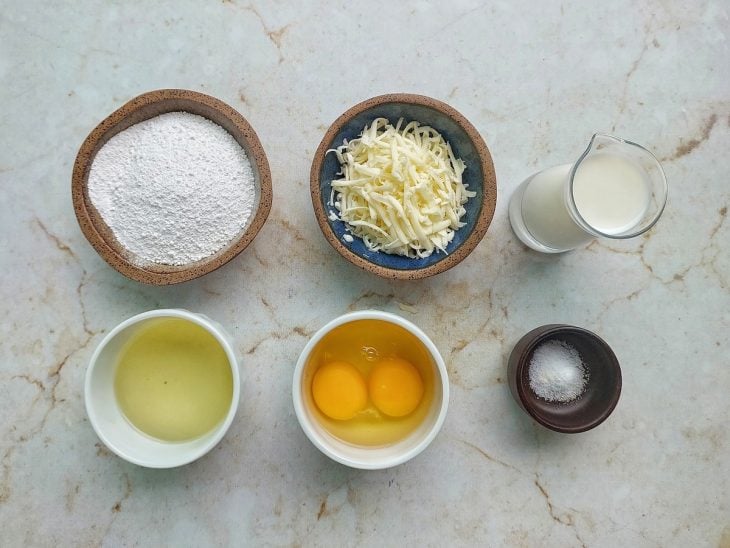 Ingredientes organizados na bancada com polvilho, ovos, leite e queijo separados.