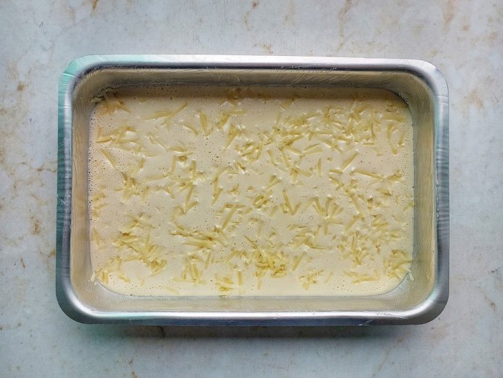 Queijo ralado sendo distribuído sobre a massa.
