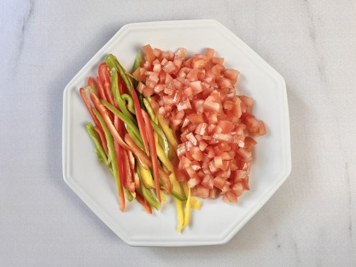 Cebolas, pimentões e tomates cortados em um pratos.