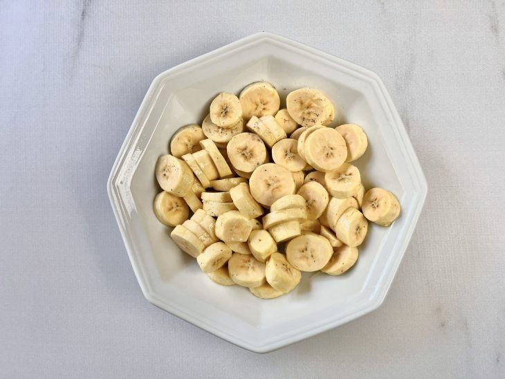 Rodelas de bananas temperadas com alho, sal, pimenta-do-reino, limão e azeite em um prato.