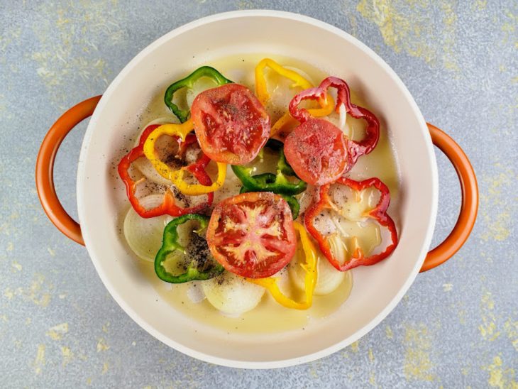Uma panela com camadas de cebola, tomate, pimentões e dedo-de-moça.