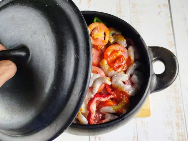 Panela com moqueca sendo tampada.