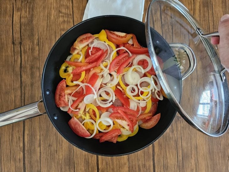 Uma panela cozinhando camadas de pimentões, cebola, postas de peixe, cebola e toamate.