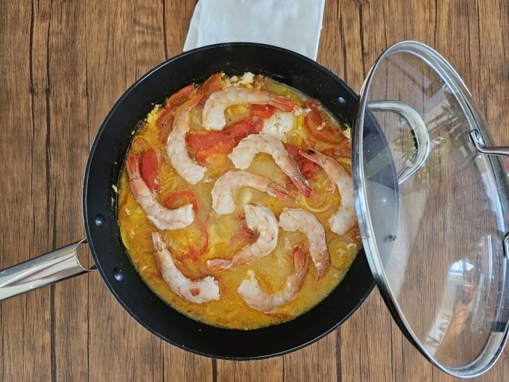 Uma panela cozinhando camadas de pimentões, cebola, postas de peixe, cebola e tomate com leite de coco e camarão.