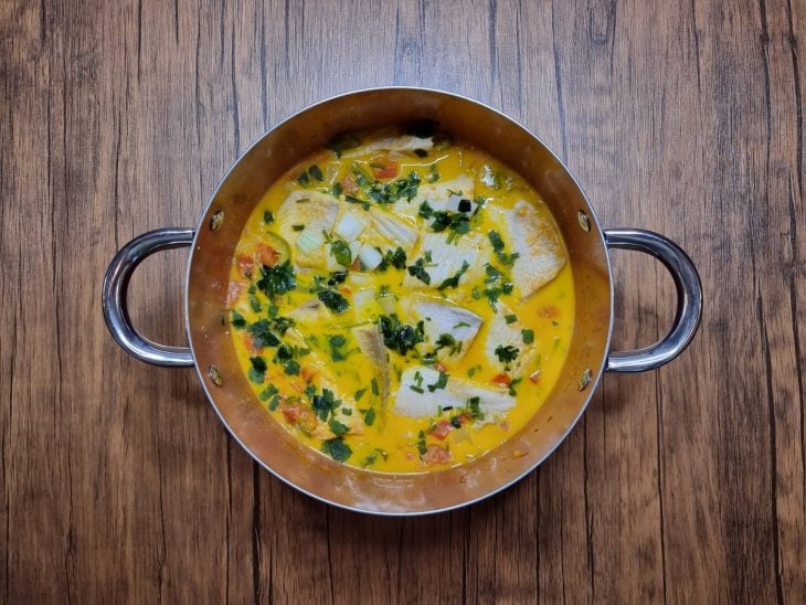 Panela com moqueca de peixe salpicada com cheiro-verde.