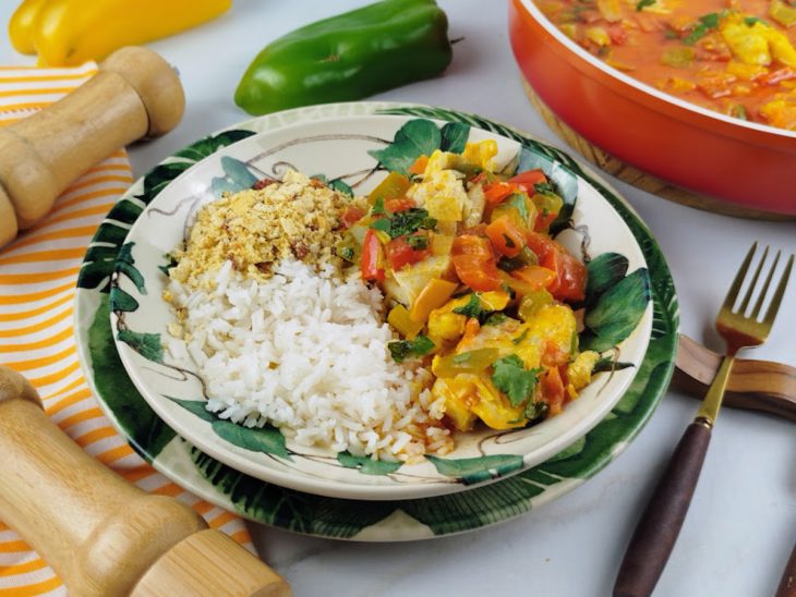 Moqueca pronta, servida em prato acompanhada de farofa e arroz branco.