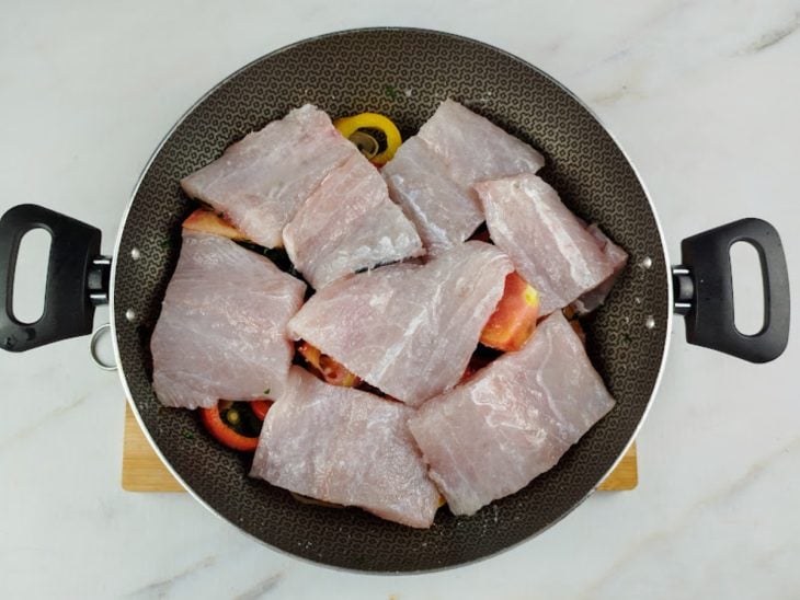 Uma panela com azeite, cebola, pimentões, sal, alho, pimenta, tomate, cebolinha, peixe.