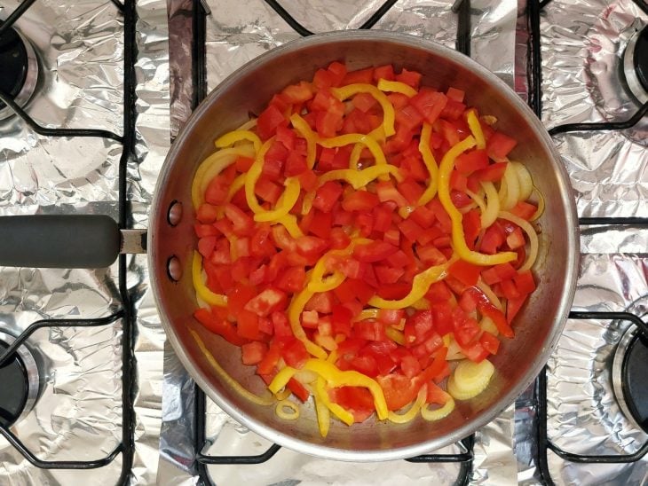 Uma frigideira refogando cebola, pimentão amarelo, pimentão vermelho e cebola.