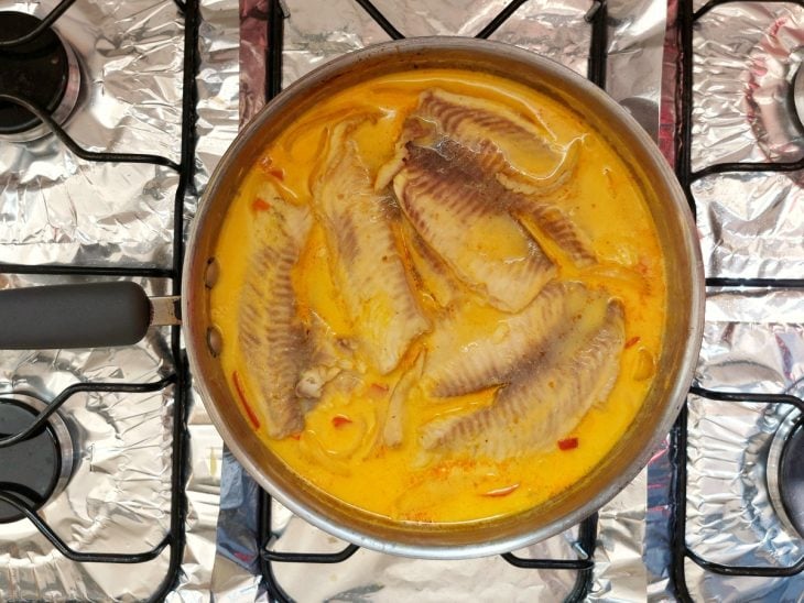 Uma frigideira refogando cebola, pimentão amarelo, pimentão vermelho, cebola, peixe e caldo.