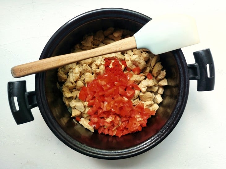 Uma panela contendo cubos de frango refogados e tomates.