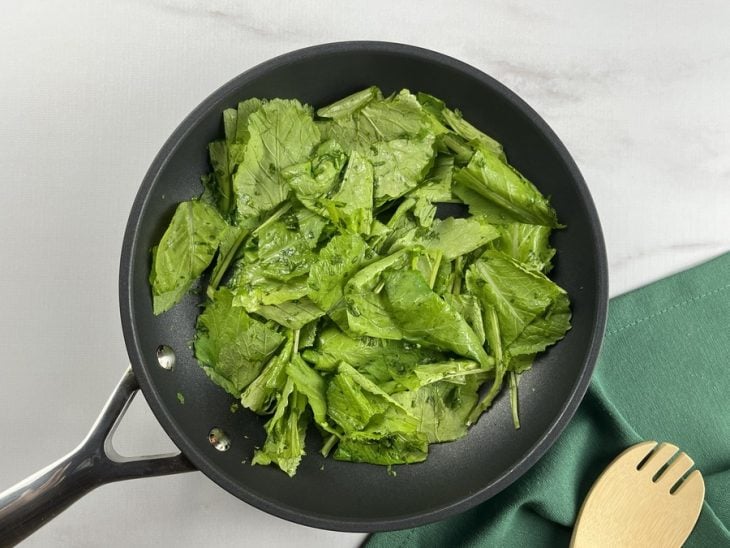 Uma frigideira refogando folhas de fmostarda.