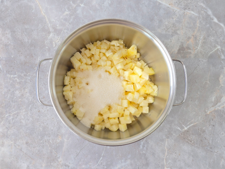 Abacaxi cozinhando com açúcar na panela até reduzir o líquido.