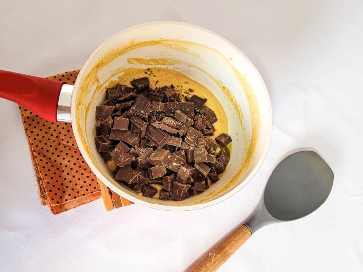 Chocolate em barras adicionado à panela com creme de cor amarelada.