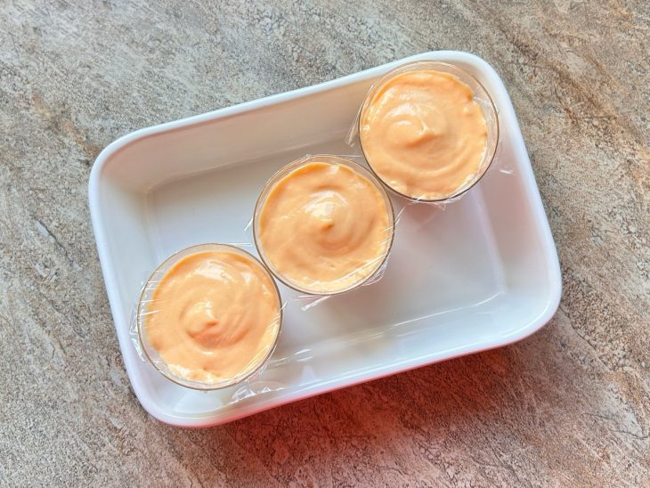 Copinhos com a mousse, dispostos dentro de uma travessa para ir à geladeira.