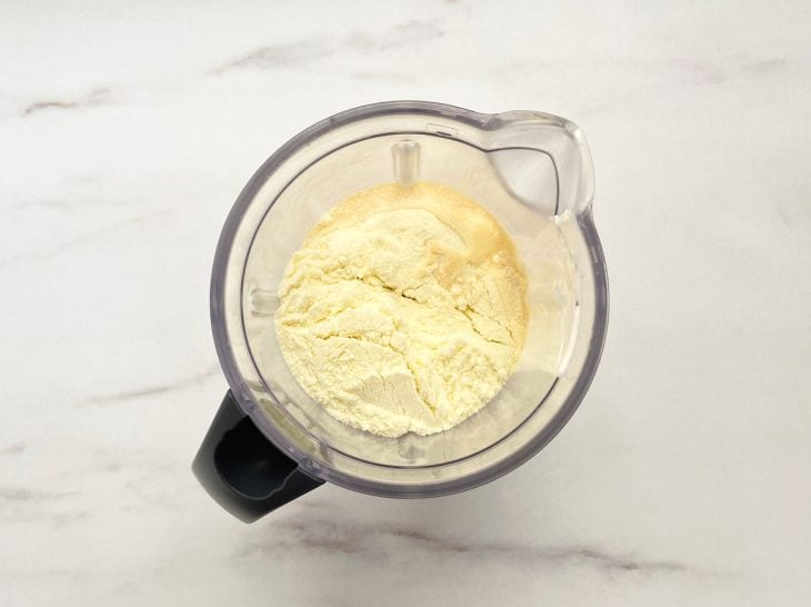 Um liquidificador com creme de leite, leite em pó, suco e leite condensado.