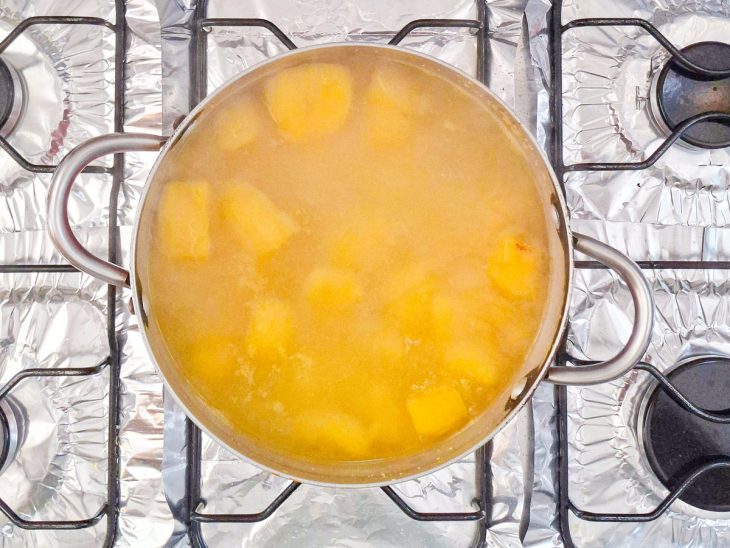 Pedaços de mandioquinha sendo cozidos em água quente numa panela.