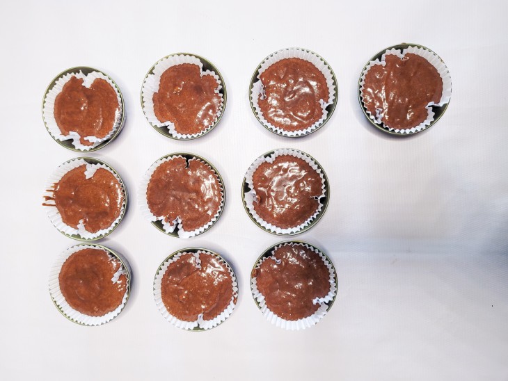 Uma bancada contendo forminhas de cupcake com massas de muffins cruas.