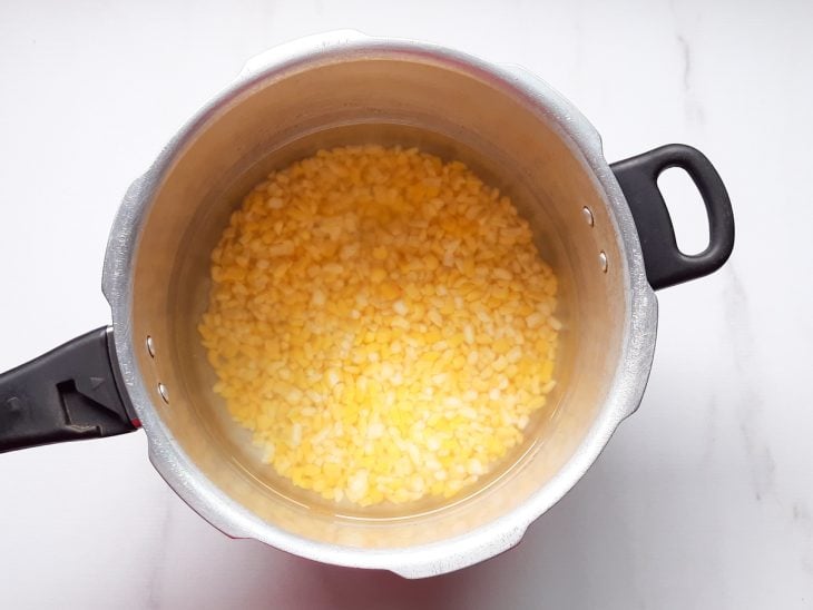 Uma panela de pressão contendo milho amarelo coberto com água.