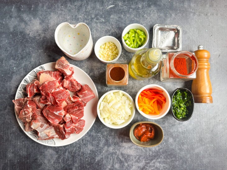 Ingredientes organizados na bancada com carne cortada, legumes e temperos separados.