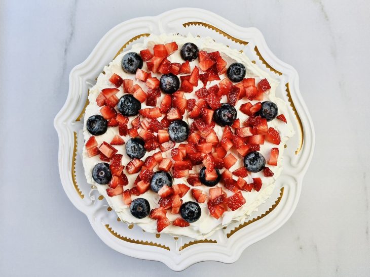 Creme branco e frutas vermelhas picadas espalhadas sobre a base de bolo.