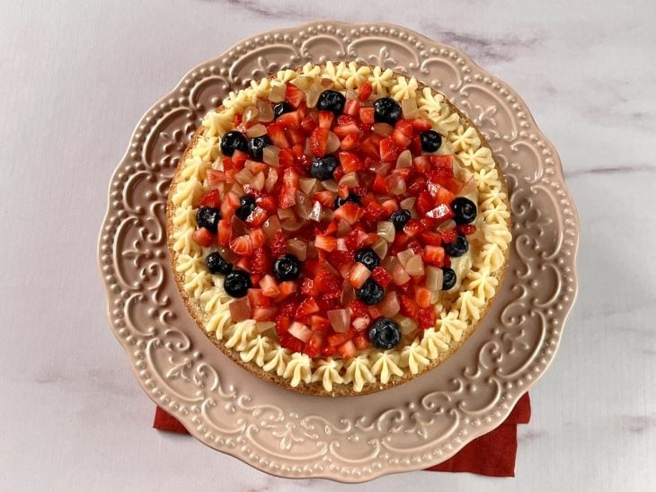 Uma parte de bolo coberto com brigadeiro branco e frutas vermelhas.