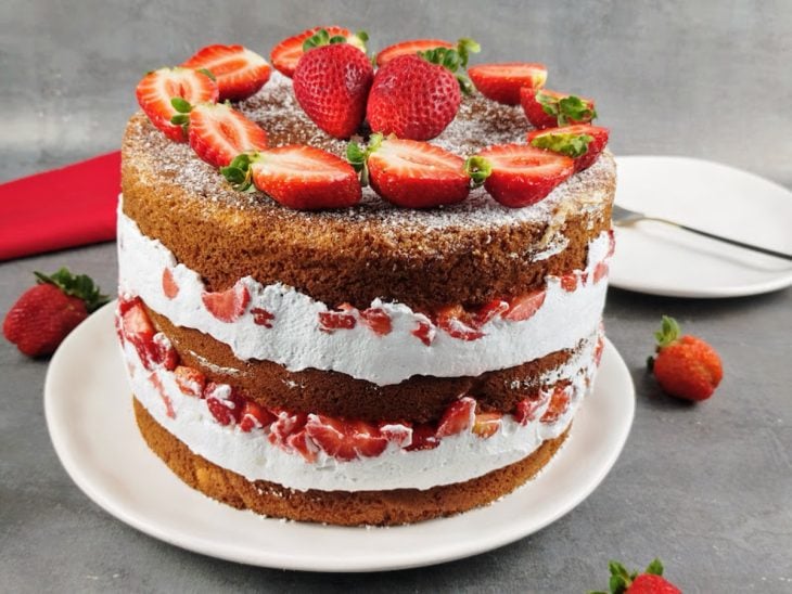 Naked cake decorado com açúcar de confeiteiro e morangos por cima pronto para consumo.